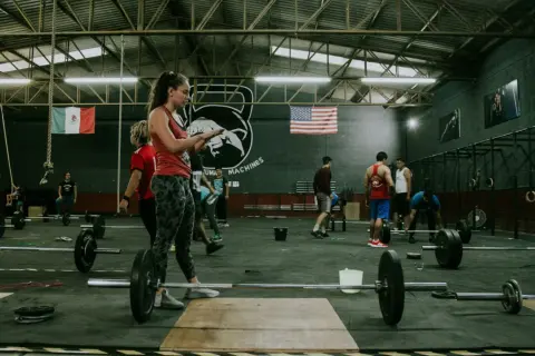 Ludzie trenujący crossfit w siłowni z flagami Meksyku i USA w tle.