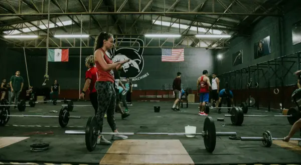 Ludzie trenujący crossfit w siłowni z flagami Meksyku i USA w tle.