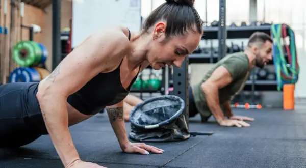 Kobieta i mężczyzna wykonują pompki na siłowni CrossFit.