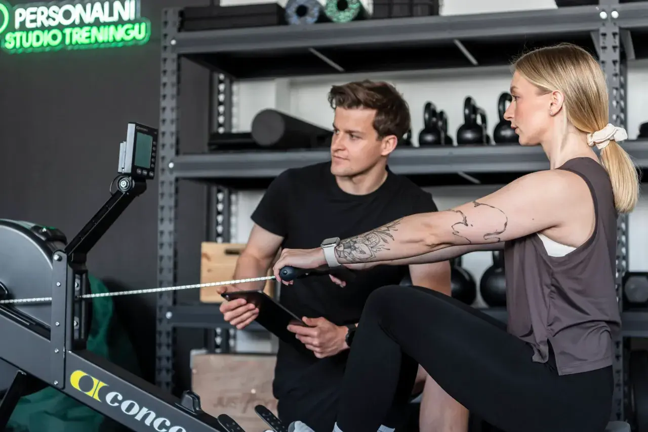Trening cardio co to? Kobieta na wioślarzu, instruktor z tabletem obok.