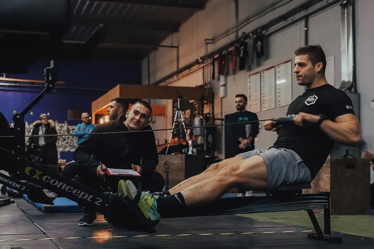 Trening na wioślarzu w stylu crossfit. Trener obserwuje zawodnika podczas ćwiczeń.