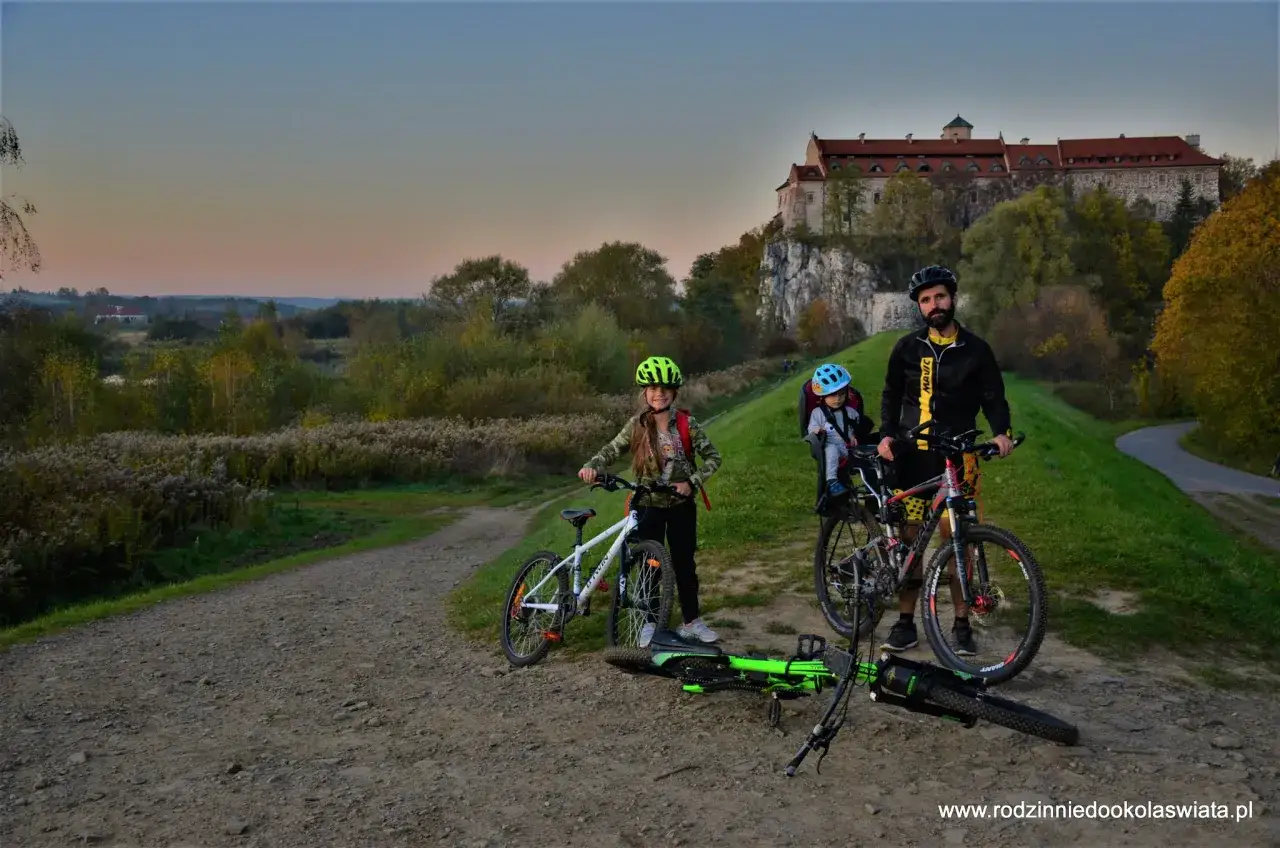Rodzina na rowerach na malowniczej wiślanej trasie rowerowej, z zamkiem w tle.