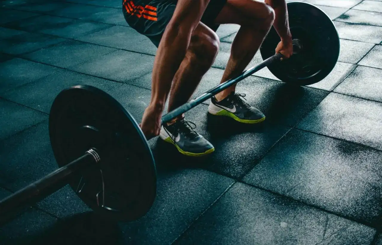 Mężczyzna w butach do crossfitu podnosi sztangę. Solidne obuwie to podstawa stabilności podczas treningu siłowego.