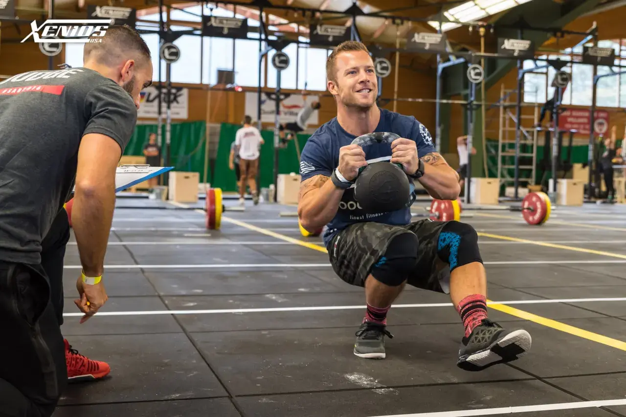 Trener obserwuje zawodnika wykonującego przysiad z kettlebell. To przykład treningu WOD CrossFit, który sprawdza siłę i wytrzymałość.